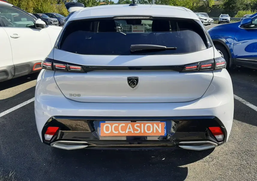 Vue arrière d'une Peugeot 308 blanche 2024 avec feux LED distinctifs et plaque "OCCASION" sur un parking.