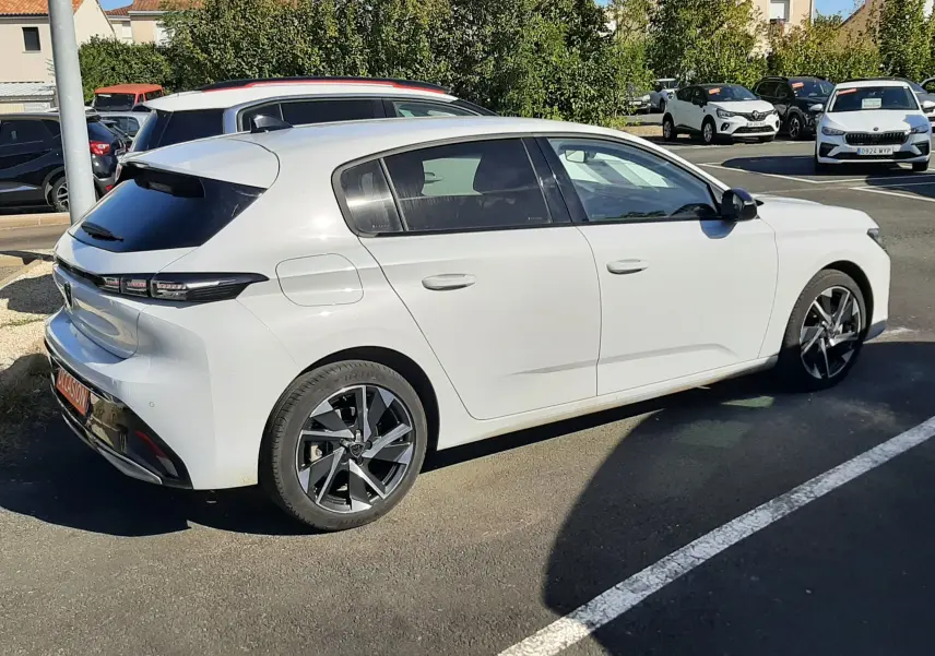 Peugeot 308 blanc vue 3/4 arrière droit, jantes alliage noires et vitres teintées, stationnée en extérieur.