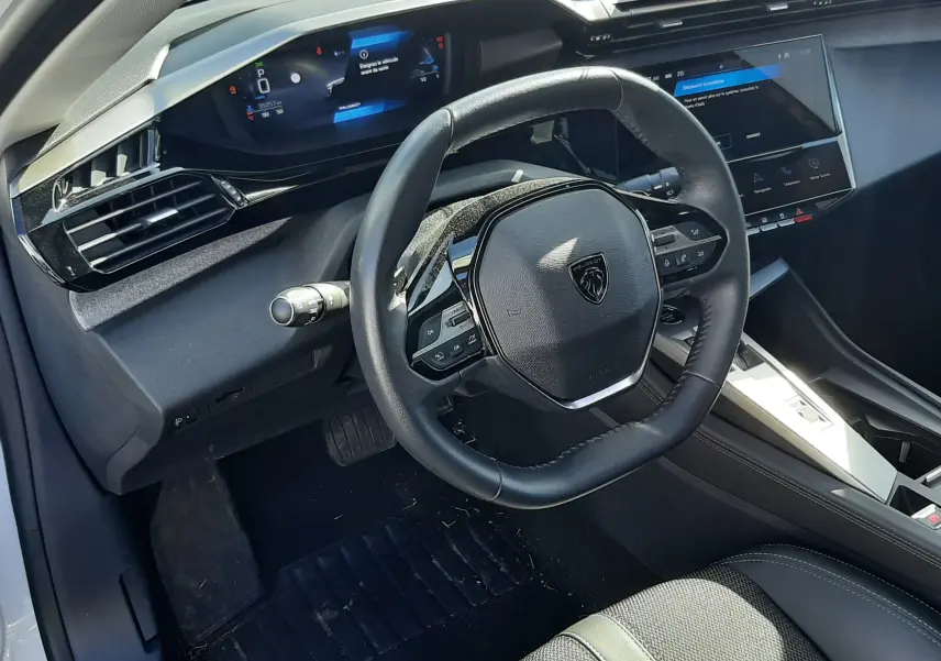 Vue intérieure côté conducteur de la Peugeot 308 2024, tableau de bord numérique et volant compact noir avec logo lion.