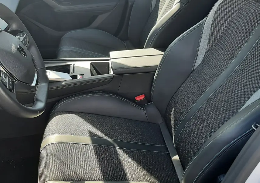 Vue intérieure côté conducteur de la Peugeot 308 2024, sièges tissu gris avec surpiqûres blanches et console centrale noire.