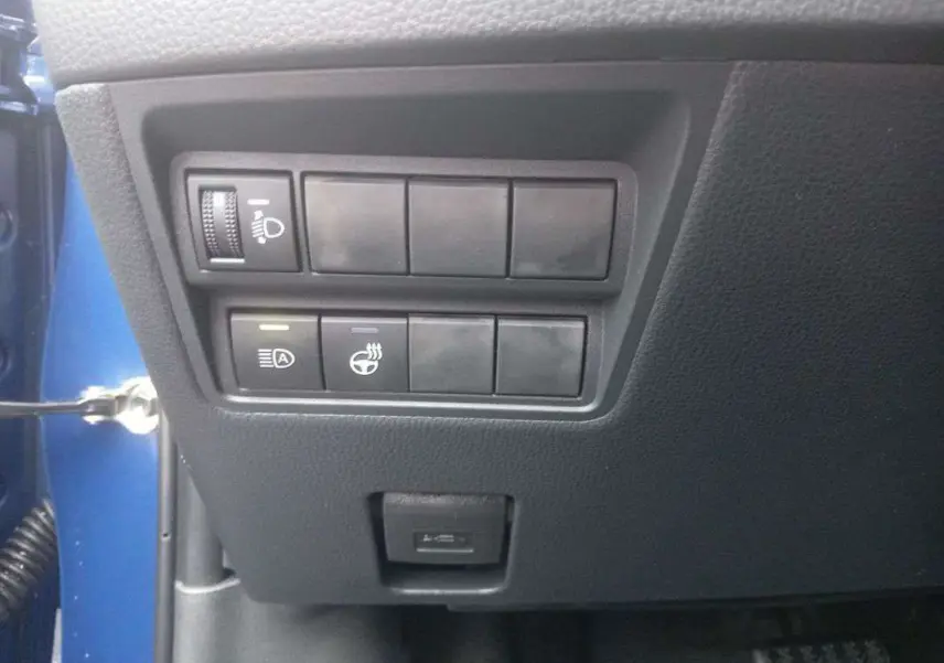 Panneau de commandes latéral gauche noir dans Toyota Yaris 1.5 Hybrid 116 BVA Design Plus 2025, avec réglage phares et fonction arrêt auto.