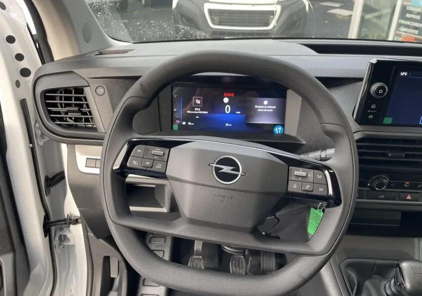 Vue intérieure centrée sur le volant noir d’un Opel Vivaro blanc 2024 avec combiné numérique et levier de vitesse manuel.