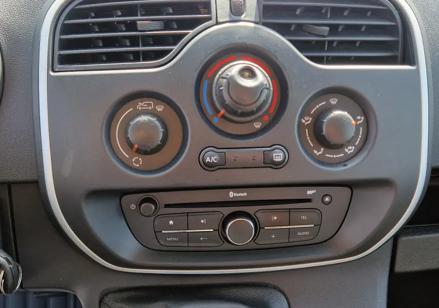 Gros plan sur la console centrale du Renault Kangoo blanc 2021, avec commandes de climatisation et radio Bluetooth.