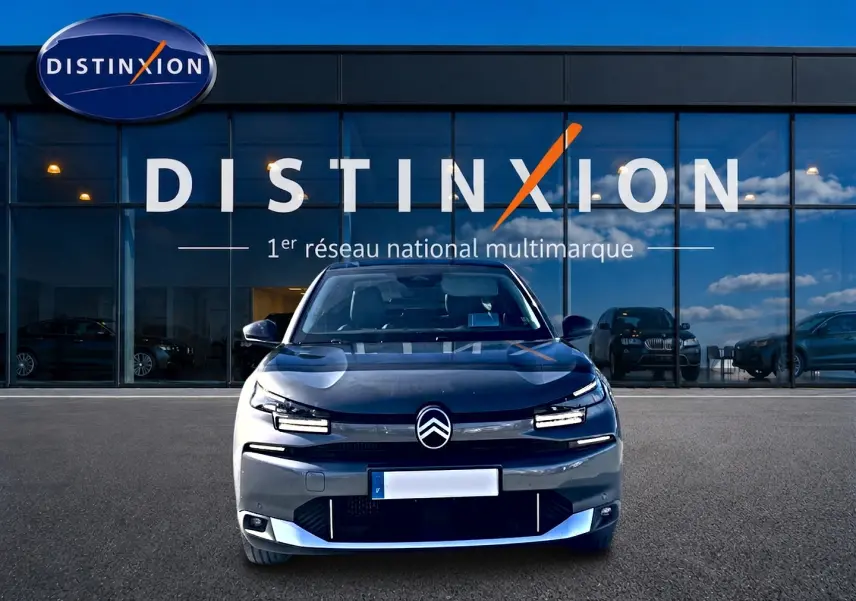 Vue frontale d'une Citroën C4 X gris mercure avec signature lumineuse LED, devant une vitrine Distinxion.