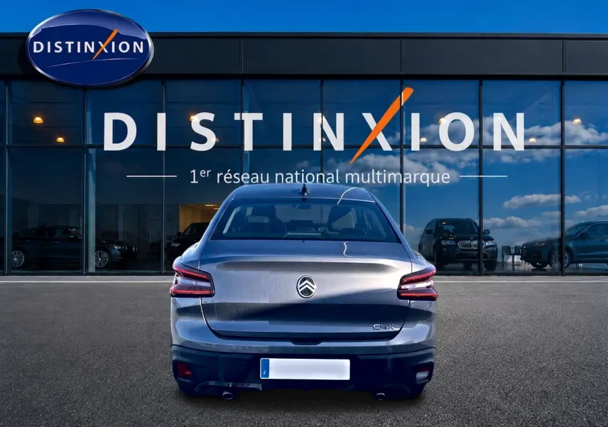 Vue arrière d'une Citroën C4 X gris mercure garée devant une vitrine avec logo Distinxion.