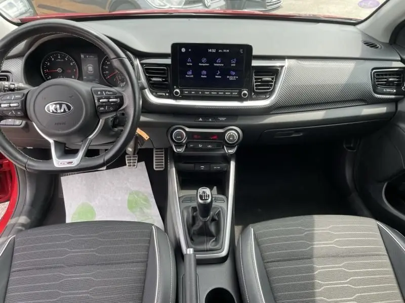Tableau de bord et volant d'une Kia avec écran tactile, sièges tissu et levier de vitesse manuel vus de face.