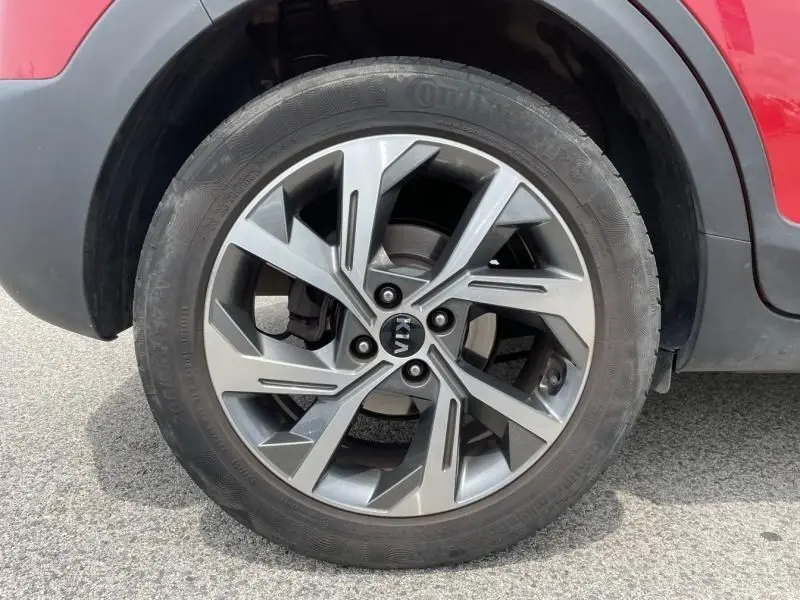 Gros plan sur la roue avant droite d'un véhicule rouge, jante en alliage au design moderne à cinq branches doubles.