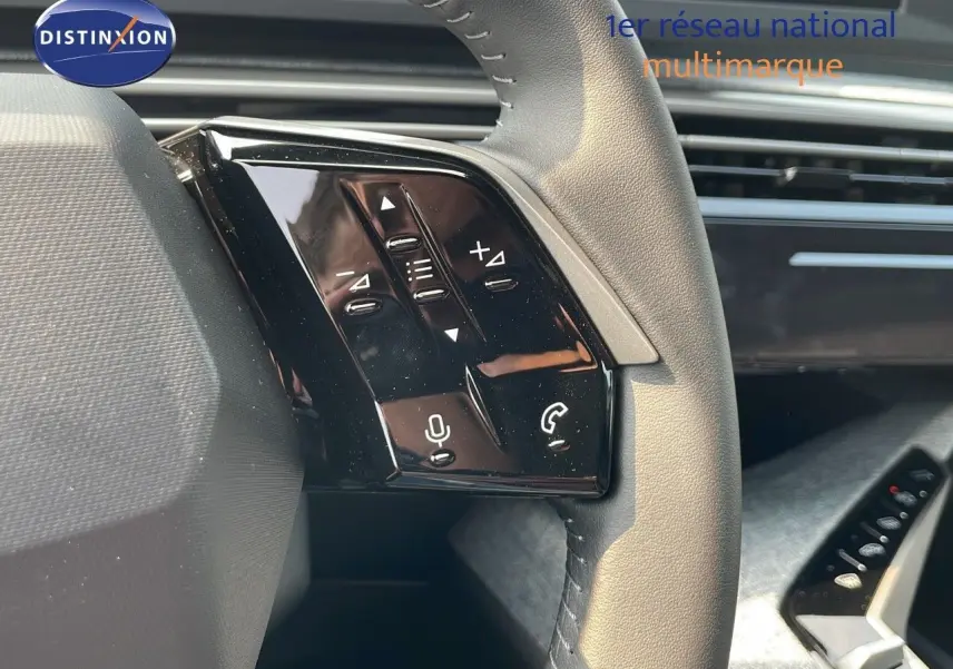 Gros plan sur les commandes gauche du volant en cuir gris du Peugeot 3008 Hybrid 2025, avec tableau de bord moderne en arrière-plan.