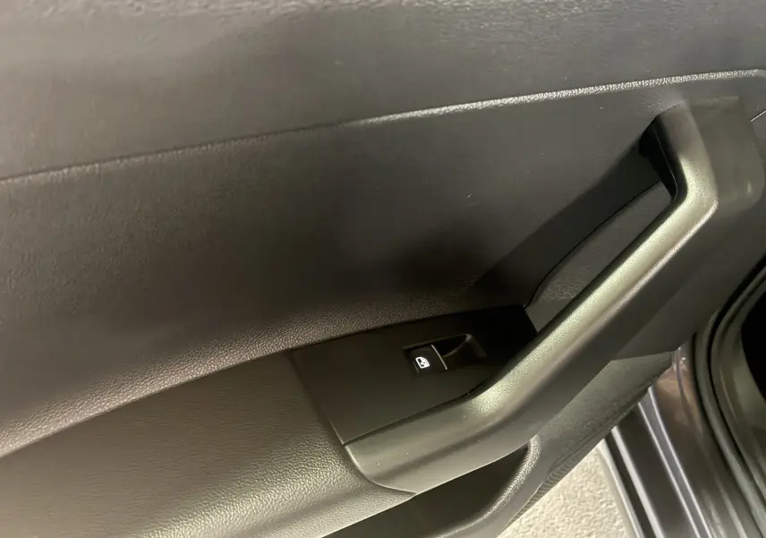 Gros plan sur la poignée intérieure et le bouton de verrouillage de la porte côté droit du Volkswagen Taigo gris 2023.