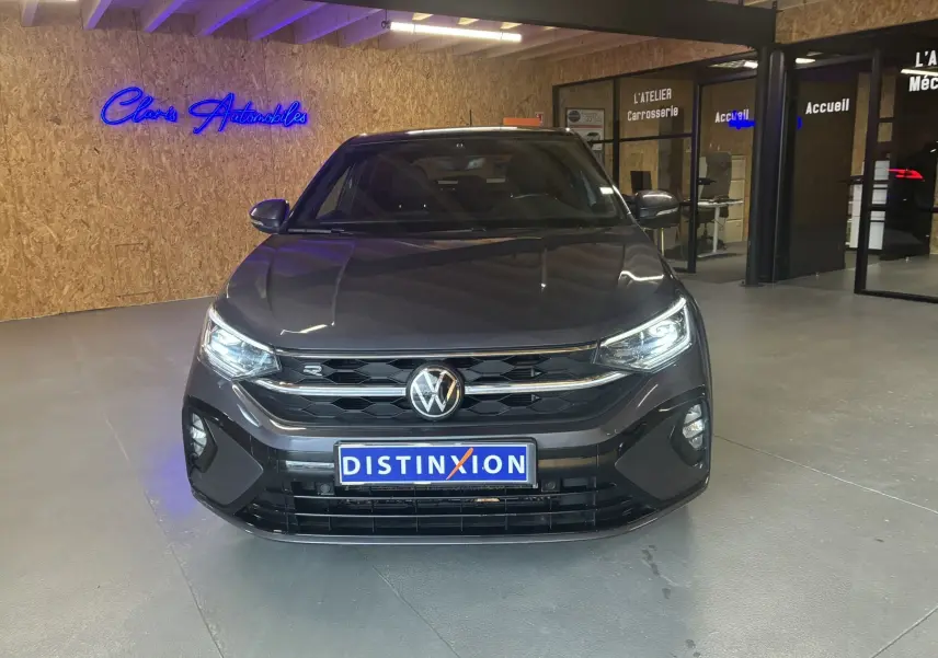 Vue de face d'un Volkswagen Taigo gris 2023 en version R-Line, avec calandre noire et phares allumés dans un showroom.