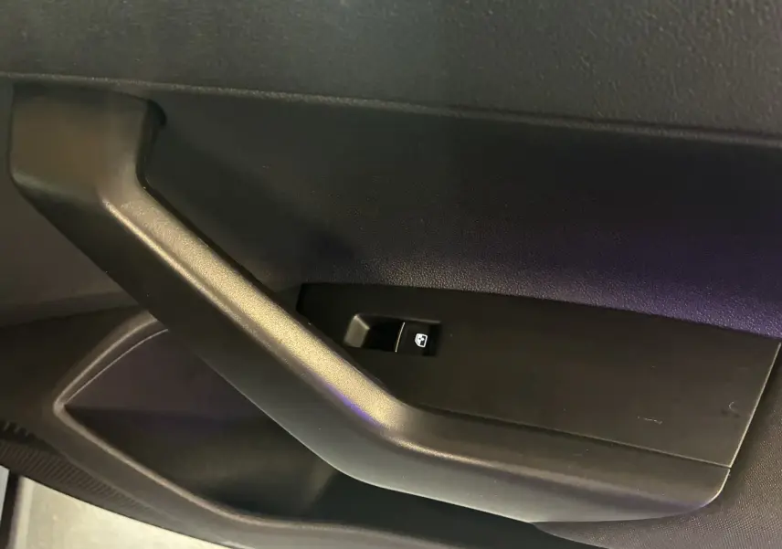 Gros plan sur la poignée intérieure noire et le bouton de commande de vitre du côté conducteur du Volkswagen Taigo gris 2023.