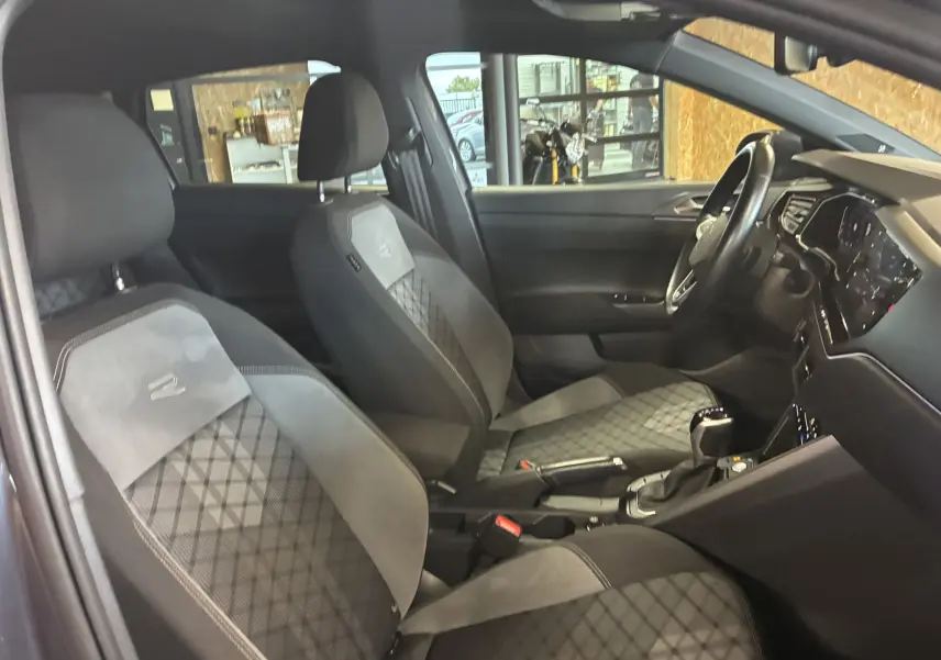 Vue intérieure côté conducteur du Volkswagen Taigo 1.5 TSI R-Line 2023 avec sièges tissu gris noir et volant multifonction.