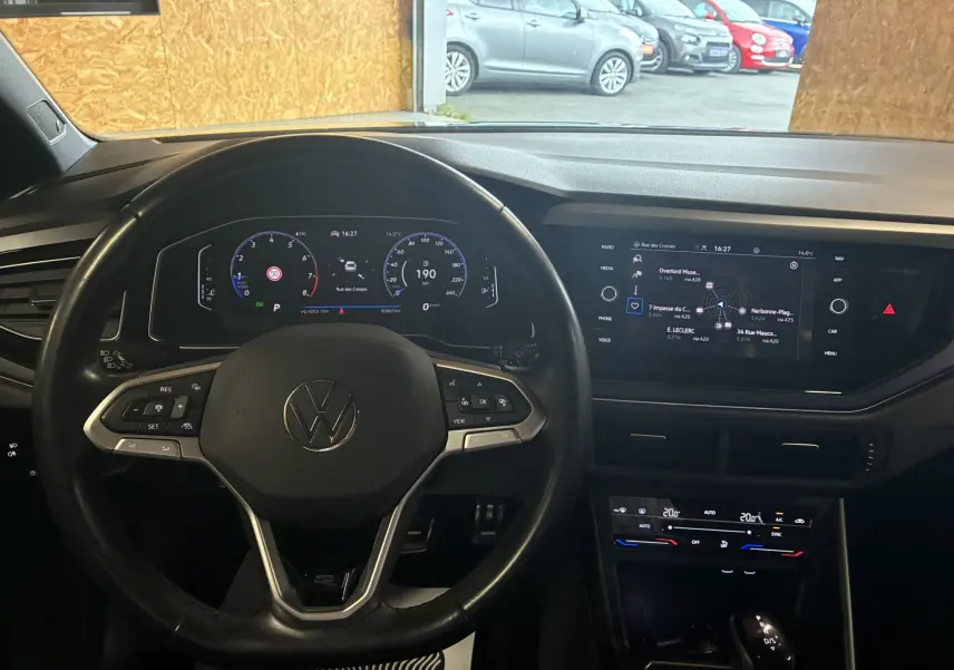 Vue intérieure du volant et tableau de bord numérique du Volkswagen Taigo gris 2023 avec écran tactile central et commandes au volant.