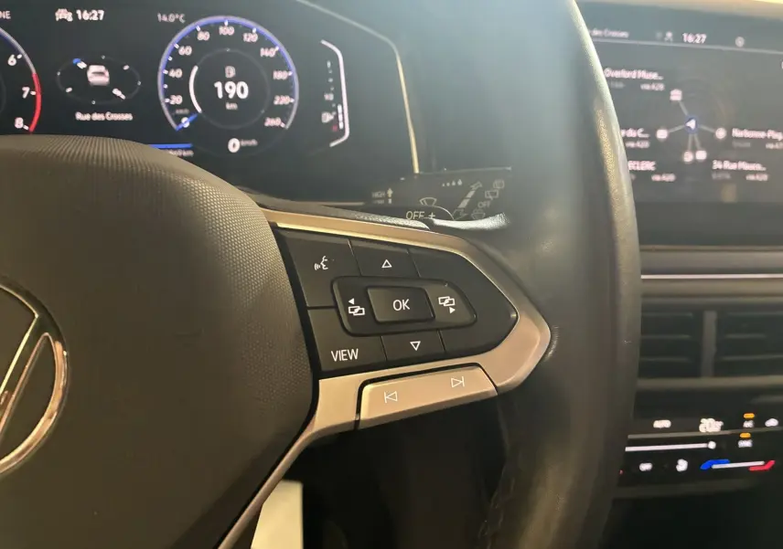 Gros plan sur le côté gauche du volant du Volkswagen Taigo gris 2023, avec commandes multifonctions et tableau de bord numérique.