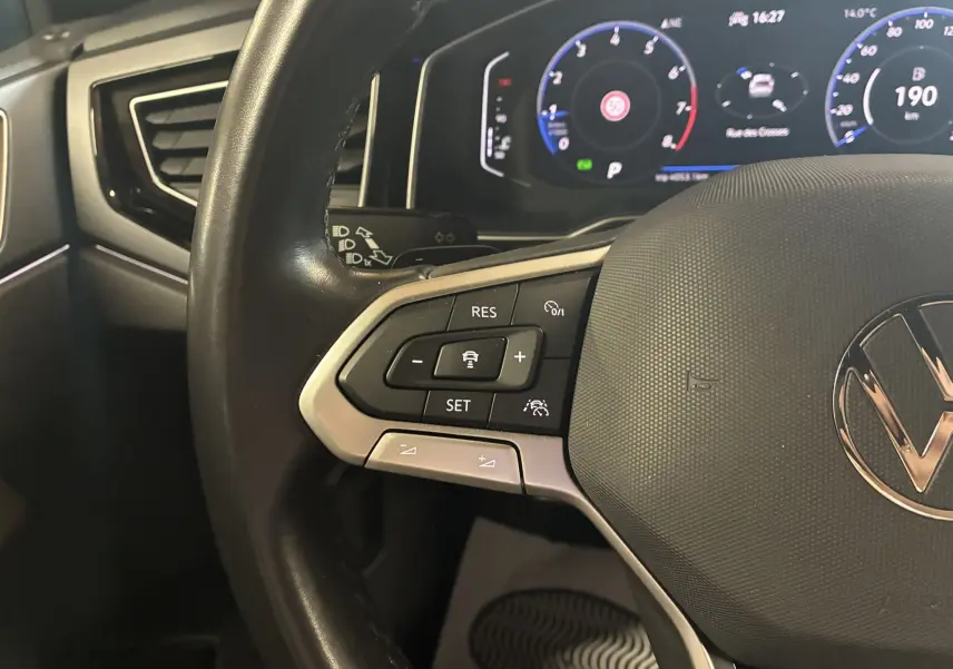 Gros plan sur le volant noir du Volkswagen Taigo 2023 avec commandes intégrées et tableau de bord numérique lumineux.