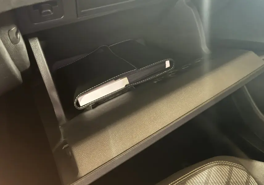 Gros plan sur la boîte à gants ouverte d'une Volkswagen Taigo gris, avec un carnet noir à l'intérieur et siège tissu gris visible.