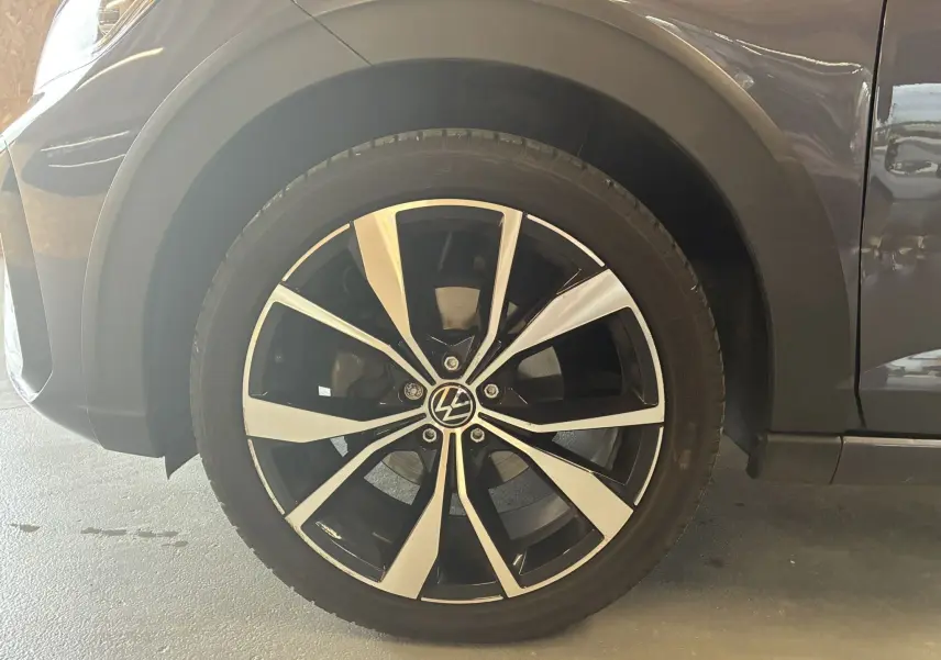 Gros plan sur la roue avant gauche du Volkswagen Taigo gris 2023, mettant en valeur la jante alliage bicolore au design dynamique.