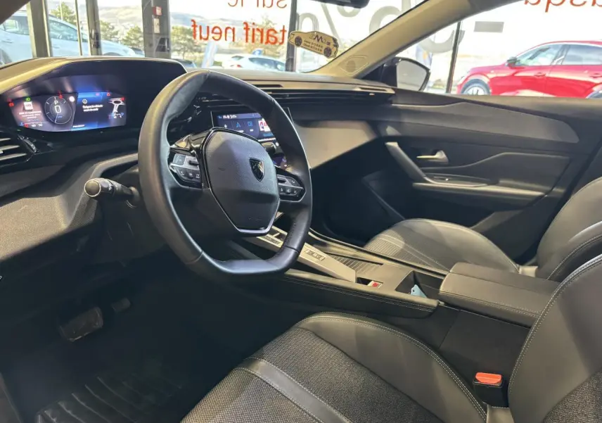 Vue intérieure côté conducteur de la Peugeot 308 SW 2024 avec volant cuir, tableau de bord numérique et sellerie tri matières noire.