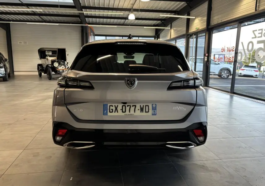Vue arrière d'une Peugeot 308 SW gris clair métallisé exposée en showroom, avec feux arrière LED et double sortie d'échappement.