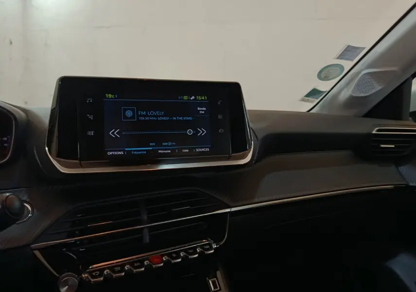 Vue intérieure du tableau de bord noir du Peugeot 208 électrique avec écran tactile central allumé.