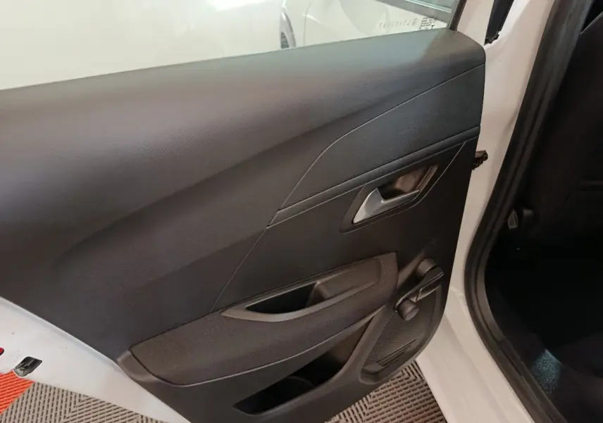 Vue intérieure sur la porte arrière droite noire d'une Peugeot 208 électrique blanche, avec poignée et manivelle de vitre.