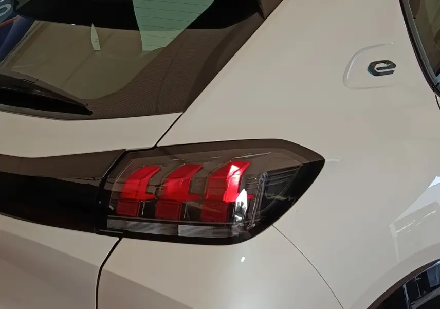 Gros plan sur le feu arrière droit rouge d’une Peugeot 208 électrique blanche, avec logo « e » sur l’aile arrière.