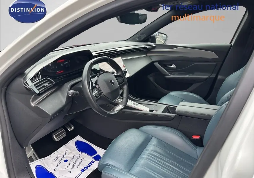 Vue intérieure côté conducteur de la Peugeot 308 SW hybride 2022, sièges cuir bleu et tableau de bord moderne.