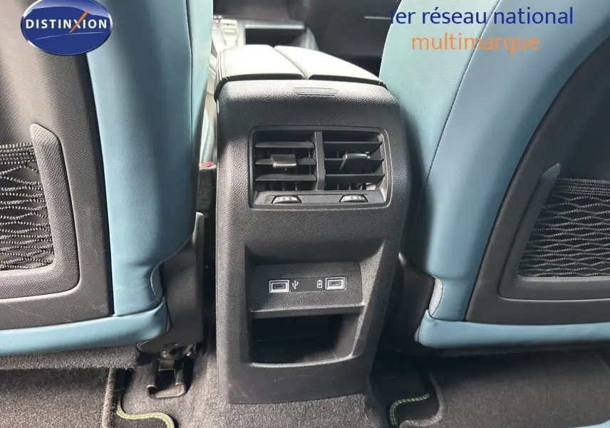 Vue rapprochée de la console arrière entre les sièges bleu clair d’un Peugeot 308 SW hybride blanc nacré, avec prises USB visibles.