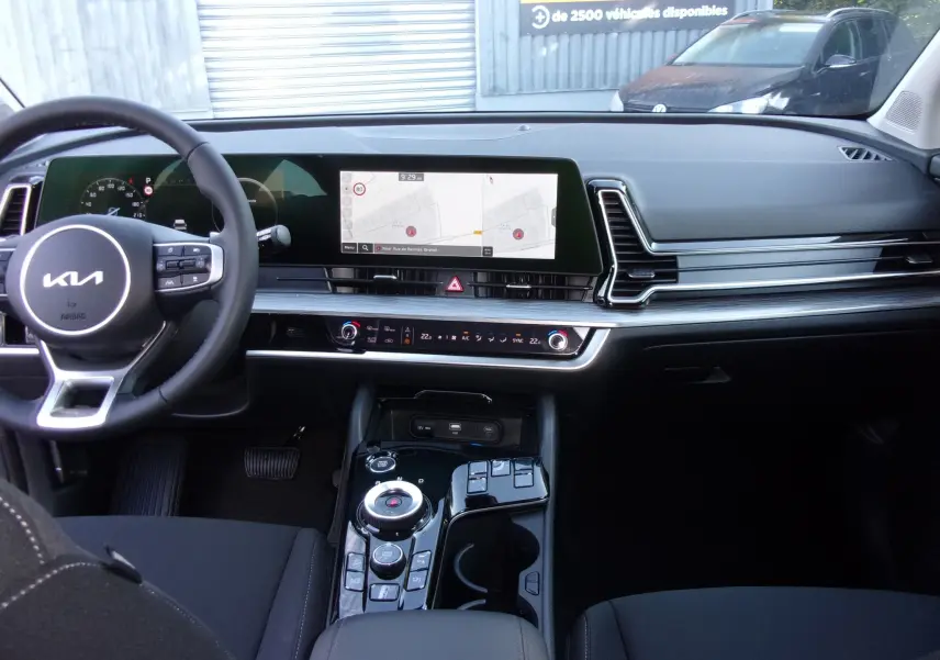 Tableau de bord et console centrale du Kia Sportage 2025 avec écran tactile GPS 12,3 pouces et volant multifonction noir.