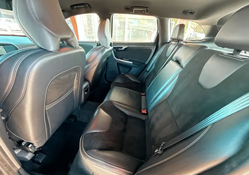 Vue intérieure arrière du Volvo XC60 gris 2016, sièges en cuir noir avec surpiqûres blanches et ceintures visibles.