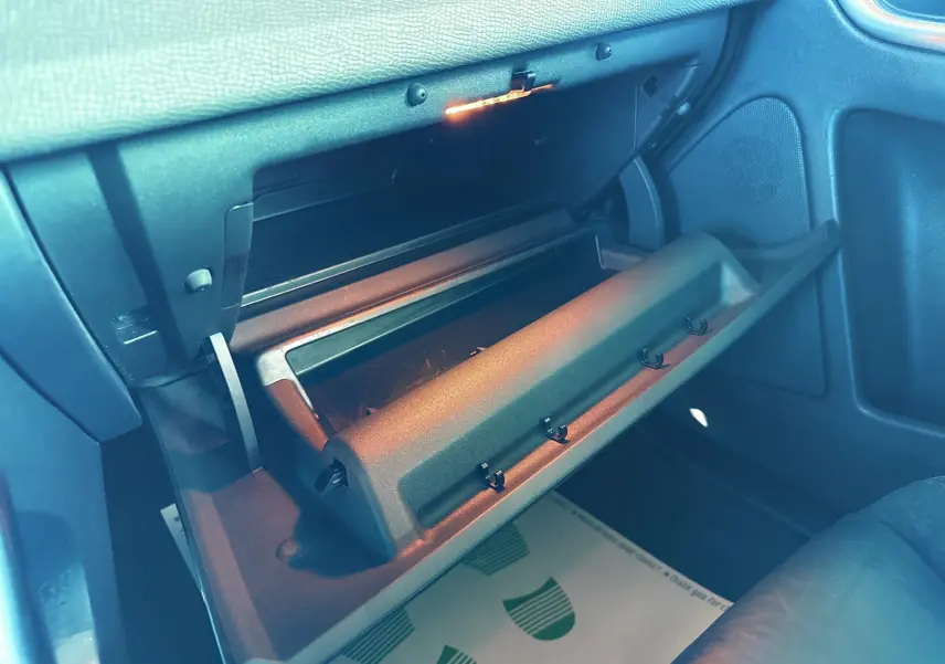 Gros plan sur la boîte à gants ouverte côté passager du Volvo XC60 gris, intérieur noir avec éclairage intérieur allumé.