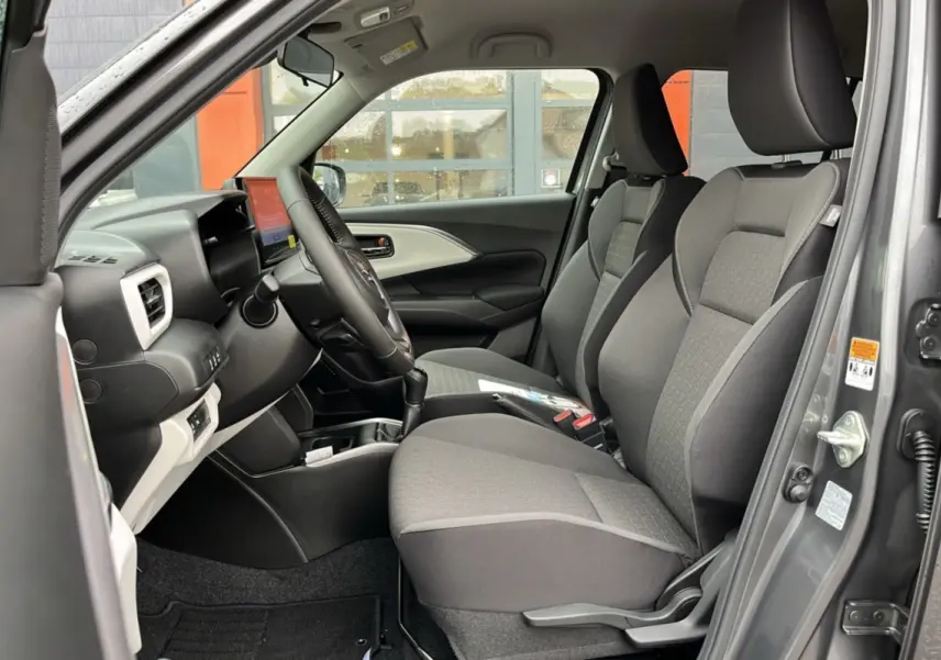 Vue côté conducteur de l'intérieur gris d'une Suzuki Swift 2025 avec sièges tissu et tableau de bord moderne.
