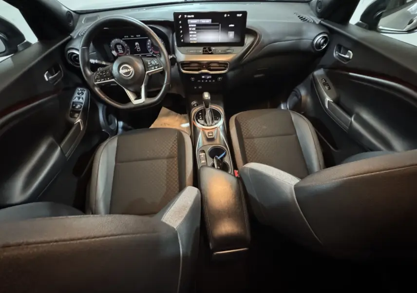 Vue intérieure avant du Nissan Juke gris clair 2025, avec tableau de bord numérique et écran tactile central.