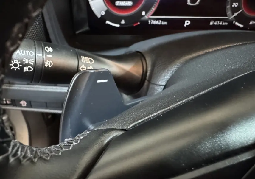 Gros plan sur la palette de changement de vitesse côté gauche du volant cuir noir du Nissan Juke gris clair 2025.