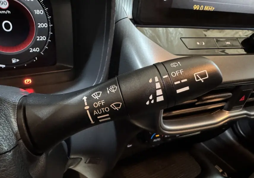 Gros plan sur la commande des essuie-glaces du Nissan Juke gris clair 2025, avec tableau de bord et écran tactile en arrière-plan.