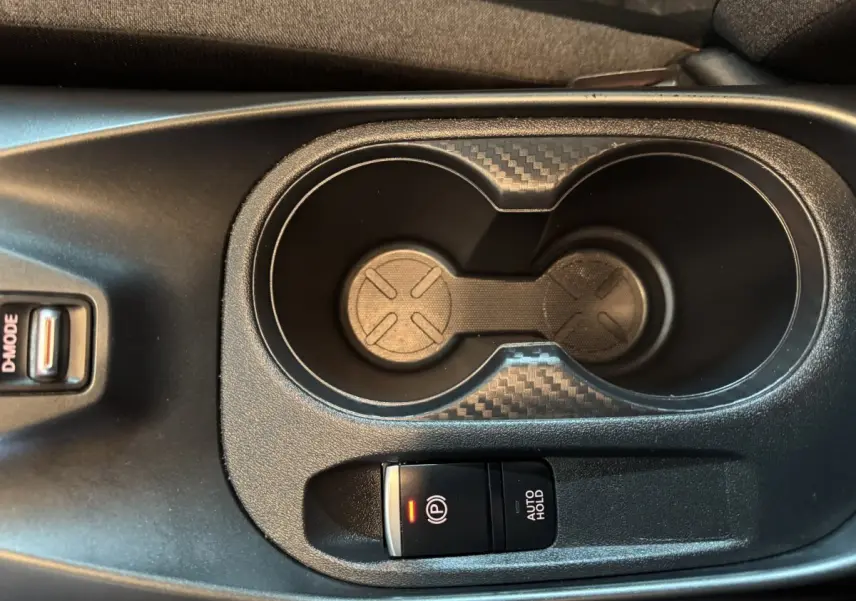 Gros plan sur la console centrale du Nissan Juke gris clair 2025, avec porte-gobelets et frein à main électrique.