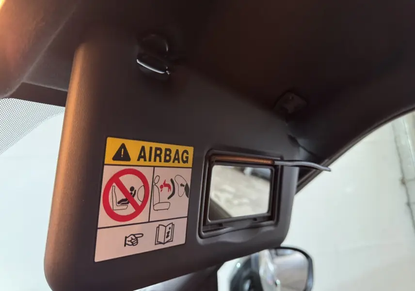 Détail du pare-soleil côté conducteur avec miroir et avertissement airbag dans un Nissan Juke gris clair.