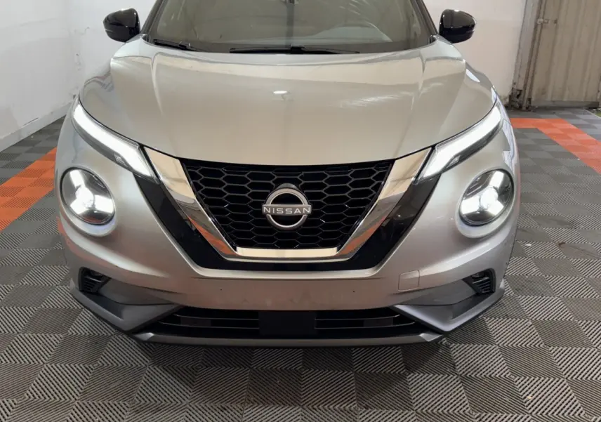 Vue frontale d'un Nissan Juke gris clair avec phares LED allumés dans un garage.