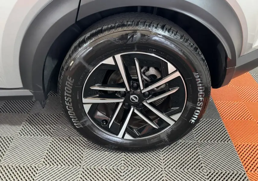 Gros plan sur la roue avant droite du Nissan Juke gris clair, mettant en valeur la jante noire et argentée au design moderne.
