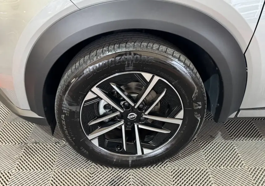 Gros plan sur la roue avant droite du Nissan Juke gris clair, mettant en valeur la jante alliage noire et argentée.