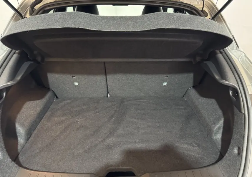 Coffre ouvert du Nissan Juke gris clair 2025, vue de l'arrière montrant l'espace de chargement vide et la tablette arrière.