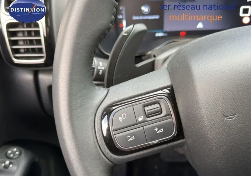 Gros plan sur les commandes au volant en cuir noir du Citroën C5 Aircross Hybrid gris platinium, avec tableau de bord flou en arrière-plan.