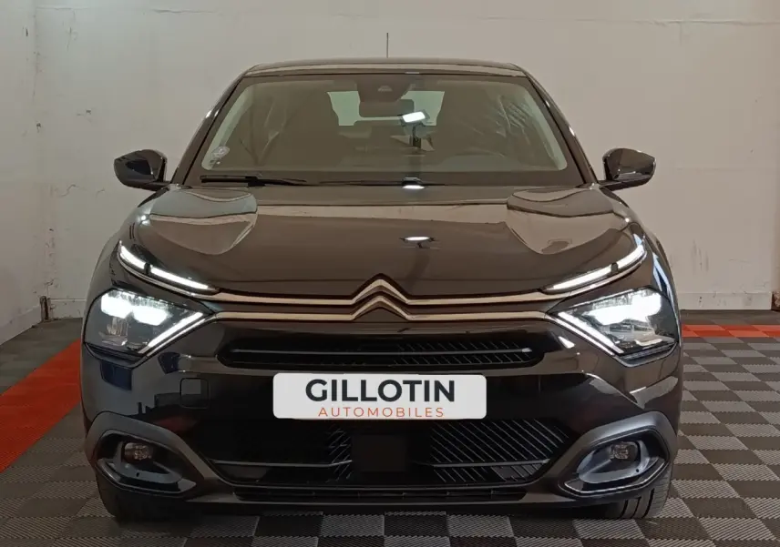 Vue frontale d'une Citroën C4 X noire 2023 avec phares LED allumés et calandre distinctive en intérieur showroom.