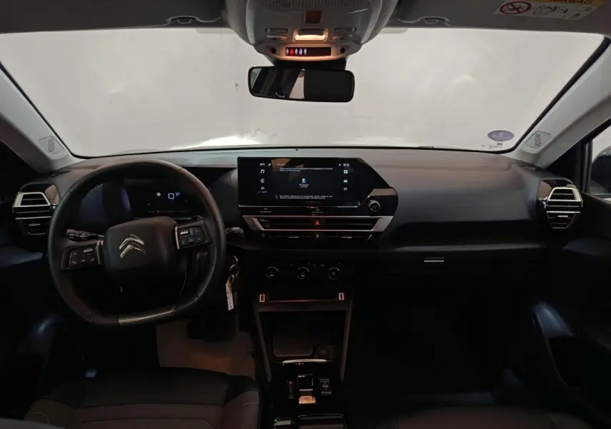 Vue intérieure avant du tableau de bord noir du Citroën C4 X 2023 avec écran tactile central et volant cuir multifonctions.