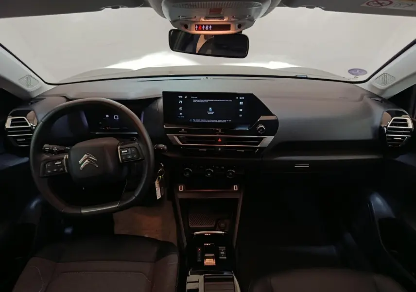 Vue intérieure frontale du tableau de bord noir du Citroën C4 X 2023 avec écran tactile central et volant multifonctions cuir.