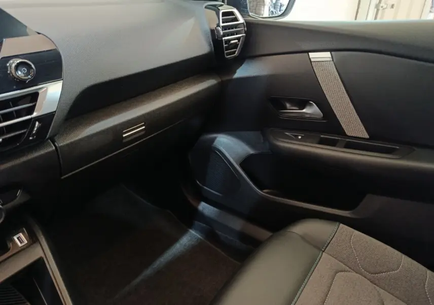 Intérieur côté passager du Citroën C4 X 2023, montrant tableau de bord et porte avec détails tissu et plastique noir.