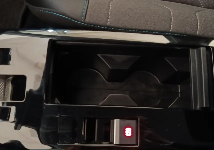 Gros plan sur la console centrale noire du Citroën C4 X avec bouton de frein à main électrique illuminé en rouge.