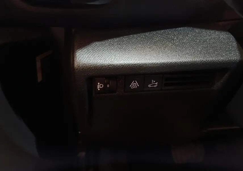 Détail des commandes d'assistance et réglage des phares sur la gauche du tableau de bord noir du Citroën C4 X.