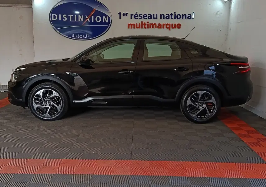 Vue latérale gauche d'une Citroën C4 X noire 2023 dans un showroom, soulignant ses lignes fluides et ses jantes modernes.