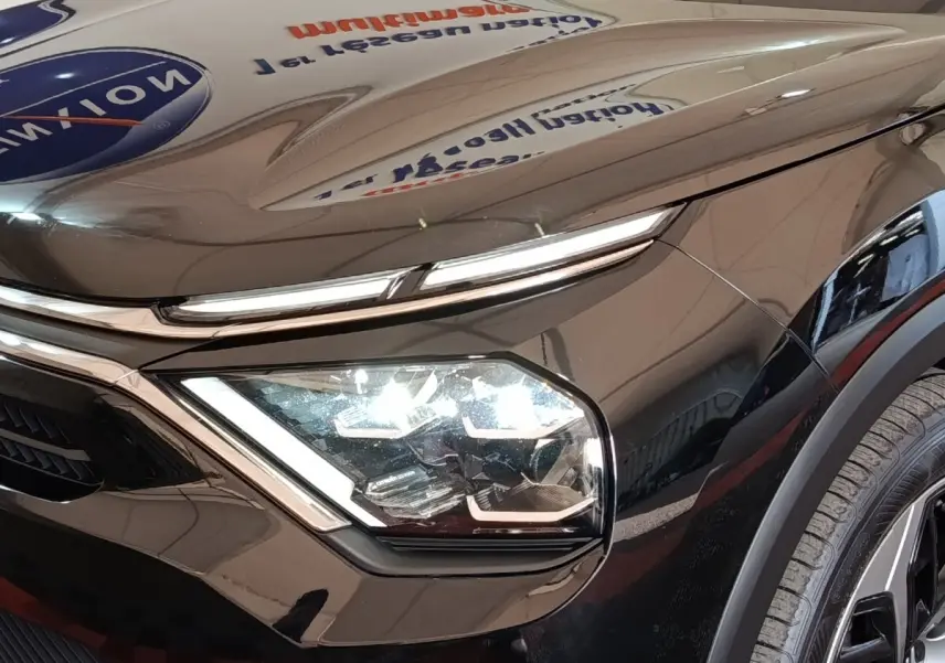 Gros plan sur le phare avant droit du Citroën C4 X noir 2023, mettant en valeur les LED et la carrosserie brillante.